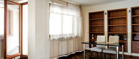 A room with a dining table, two chairs, a radiator, and wooden bookshelves.