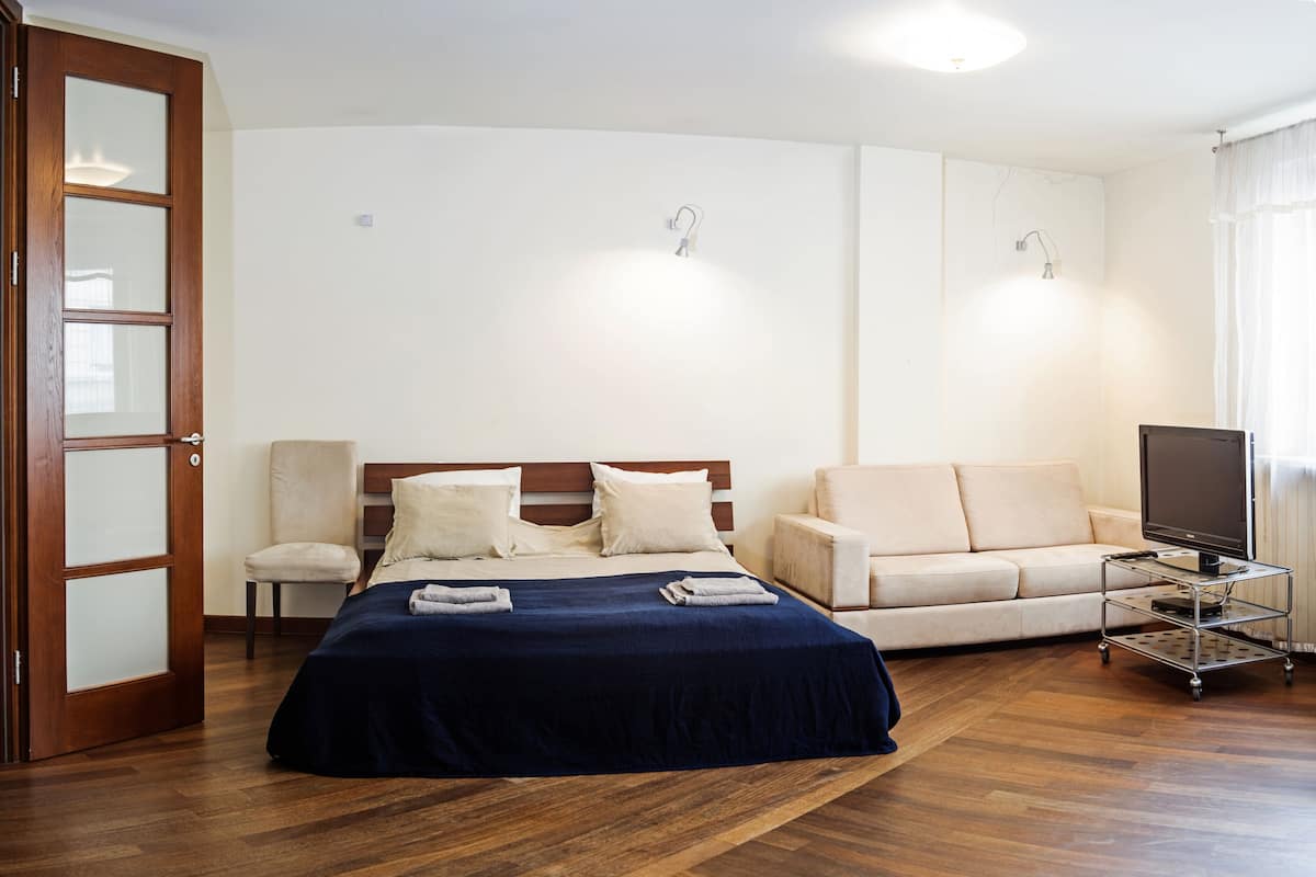 A hotel room with a bed, a sofa, a TV on a stand, and a door.