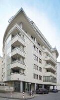 Ένα πολυώροφο κτίριο με μπαλκόνια, μια πινακίδα που αναγράφει «Szuha Residence» και αυτοκίνητα σταθμευμένα μπροστά.