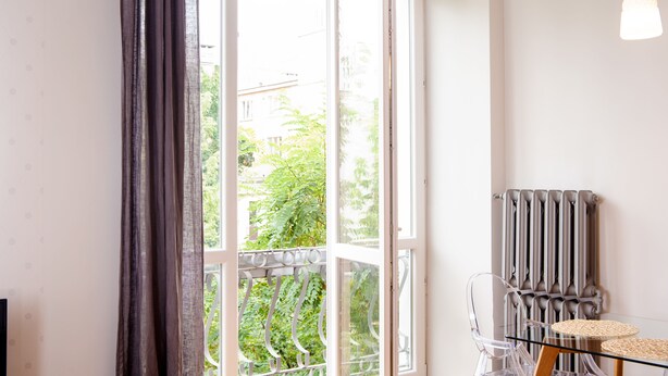 A room with a large open window, a radiator, and a glass table with chairs. - Szucha Apartments (Warsaw)
