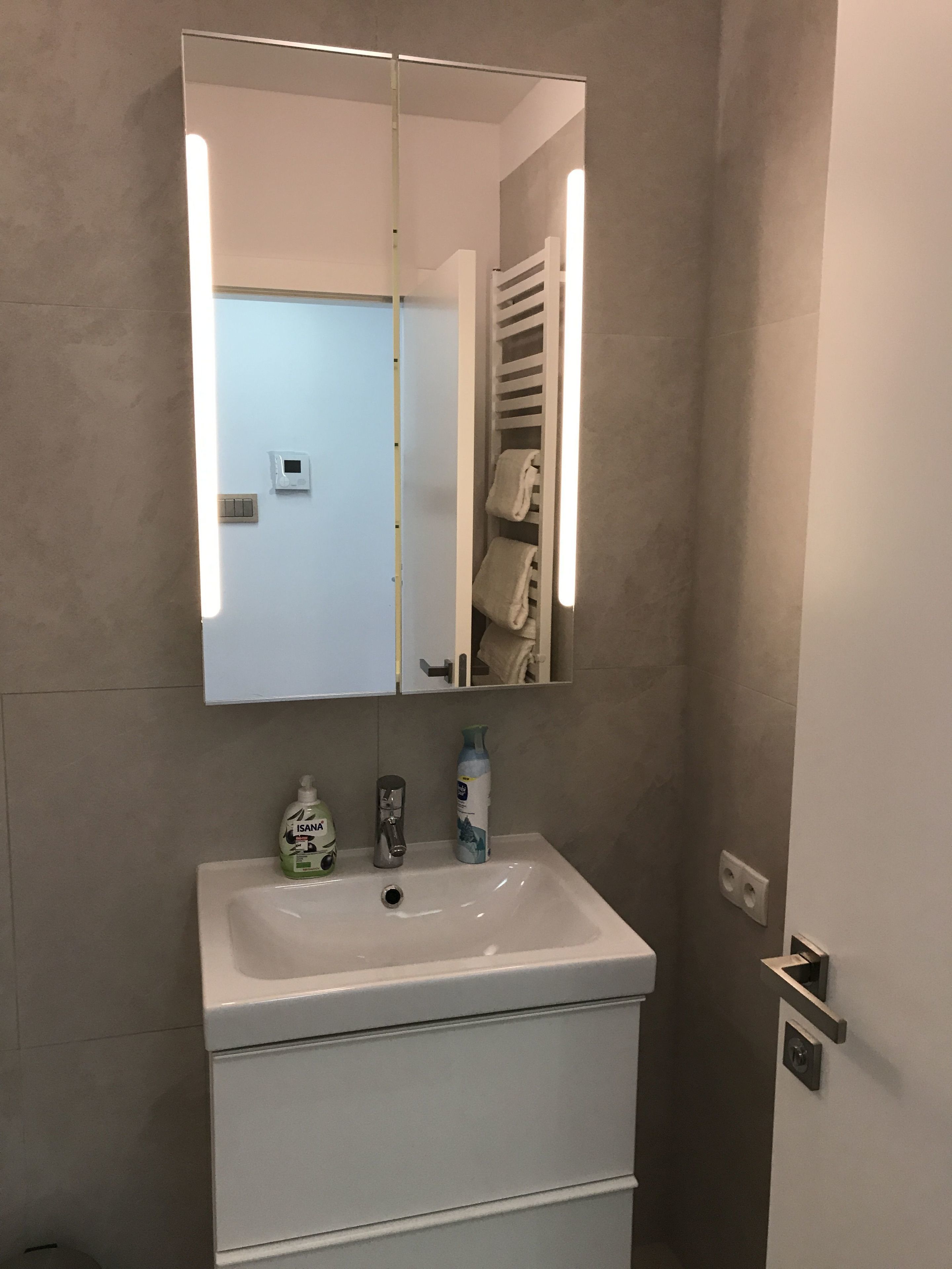 Un baño con lavamanos blanco, un espejo y un perchero para toallas.
