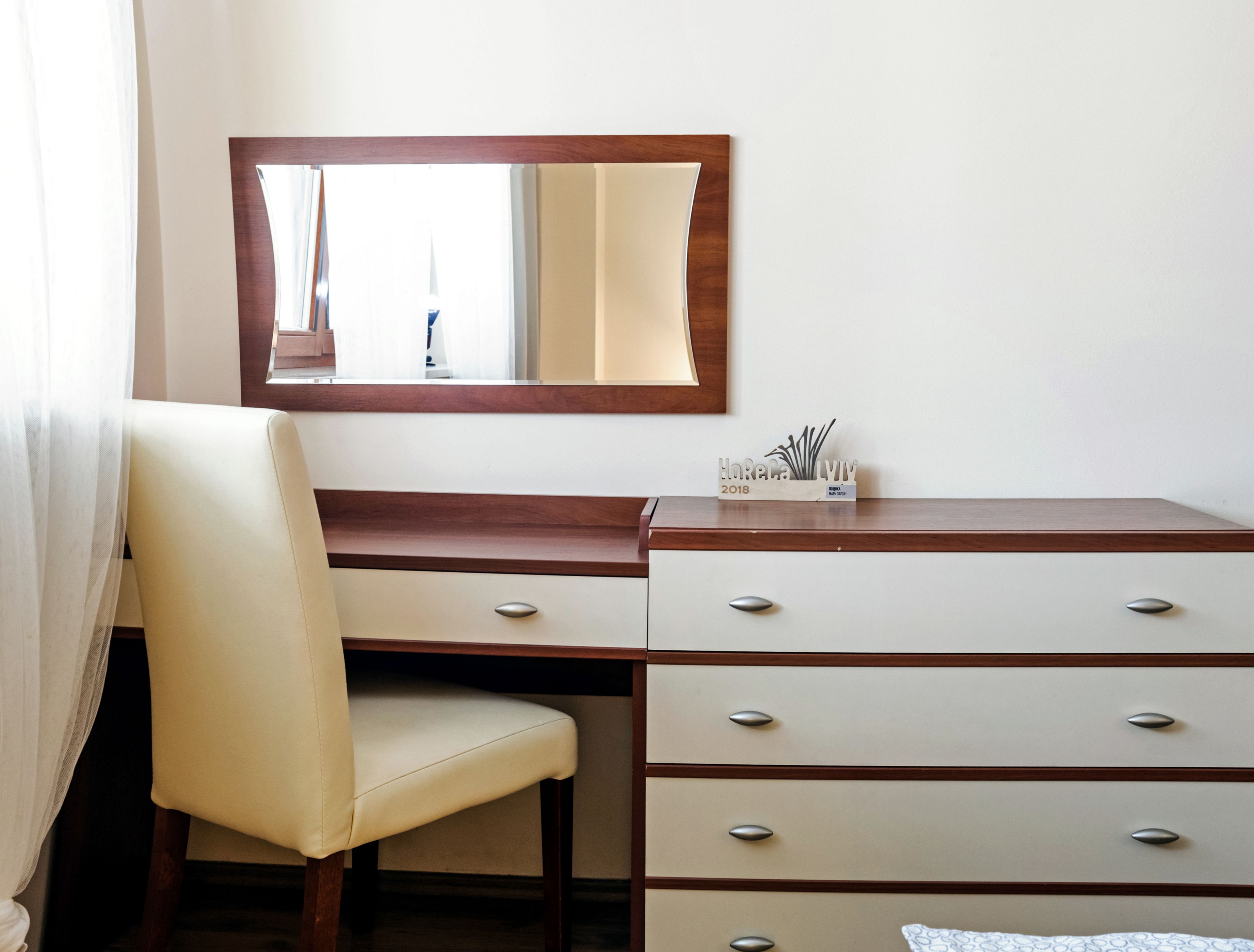 Ein Hotelzimmer mit Schreibtisch aus Holz, einem Sessel, einem Spiegel und einer Kommode mit Schubladen.