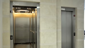 An elevator with a metallic interior and a glass door, featuring a lighted panel and a red emergency button. - Szucha Apartments (Warsaw)