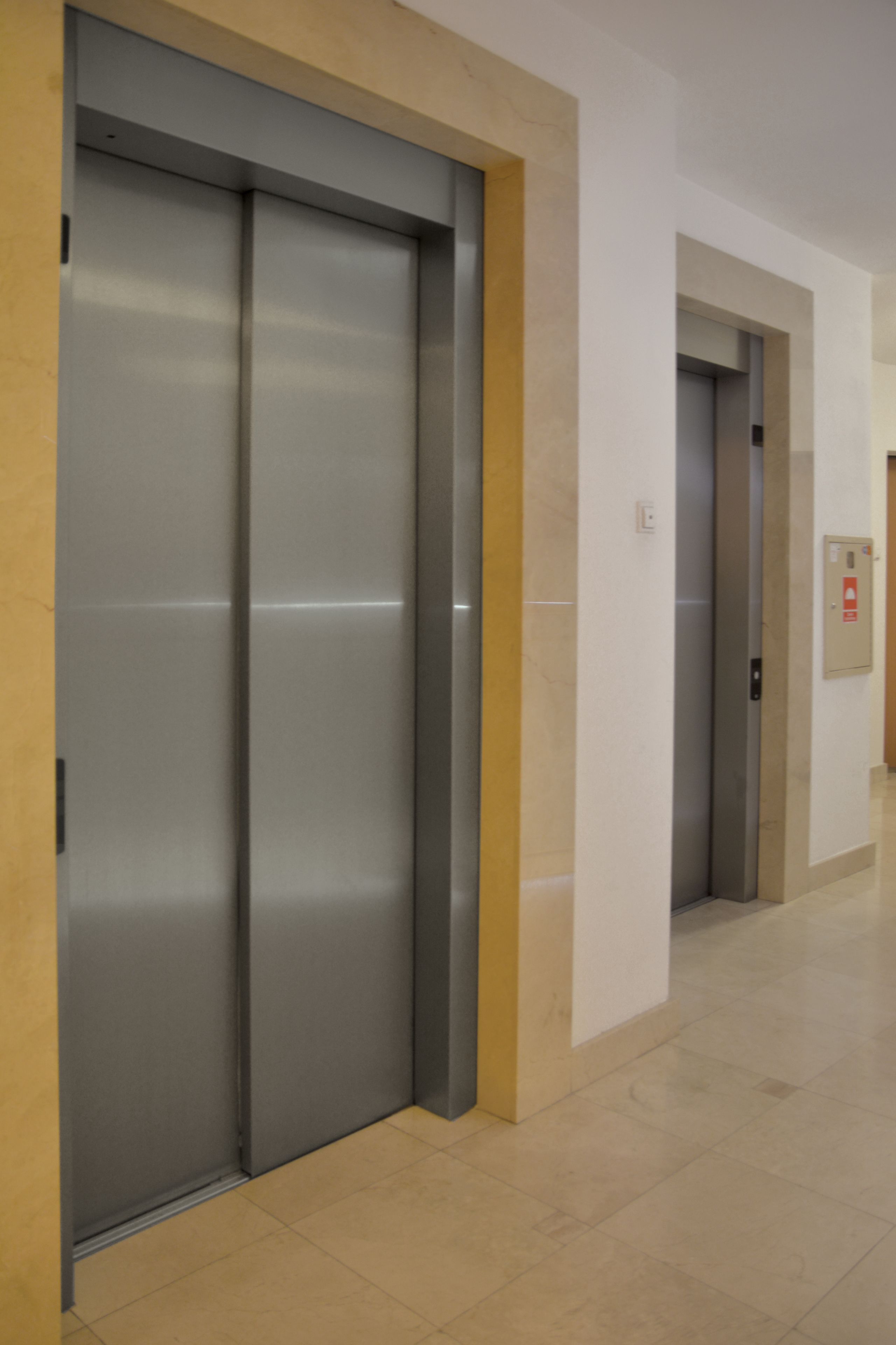 A hallway with two elevators, beige walls, and a tiled floor.