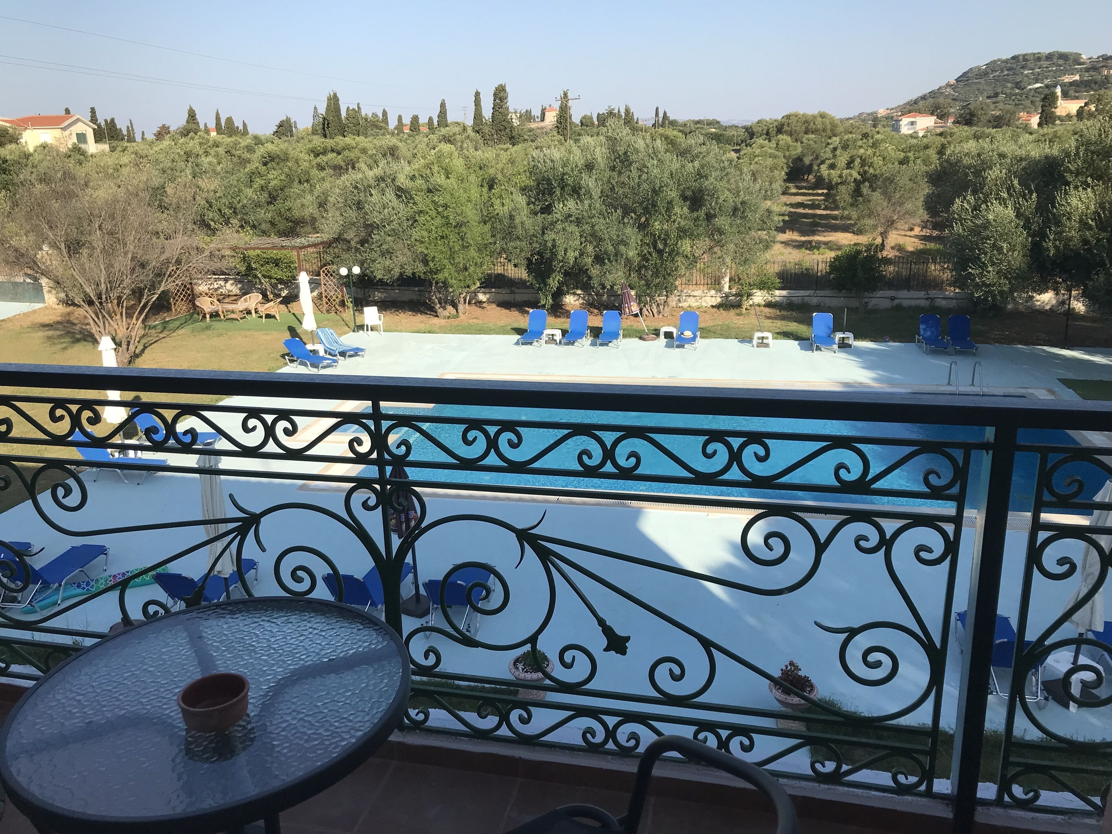 A balcony with a view of a swimming pool, lounge chairs, and a table.