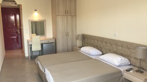 Habitación de hotel con cama doble, escritorio con silla, armario y mesita de noche con lámpara.