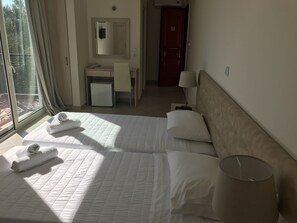 A hotel room with a bed, a desk, a chair, a lamp, and a view of the outdoors. - Ai - Helis Resort Hotel (Kefalonia)