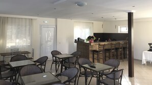 Un comedor con mesas y sillas, una zona de cocina con barra, y una puerta con interruptor de luz.