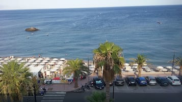 Un aparcamiento frente a la playa con coches, una zona peatonal y sombrillas.