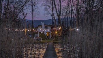 A pathway leading to a building surrounded by trees and a body of water reflecting lights.