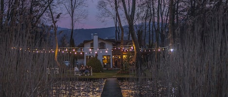 A pathway leading to a building surrounded by trees and a body of water reflecting lights.