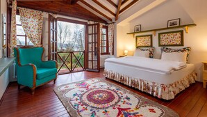 A bedroom with a large bed, a teal armchair, a patterned rug, wooden beams, and a view through a glass door. - Beta Home Lake House (Sapanca)