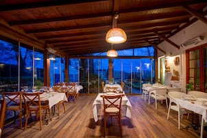 A dining area with tables and chairs, large windows, and a wooden ceiling.