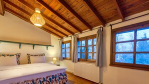 A bedroom with a wooden ceiling, a bed with a patterned bed skirt, a bedside table with a lamp, and a window with curtains. - Beta Home Lake House (Sapanca)