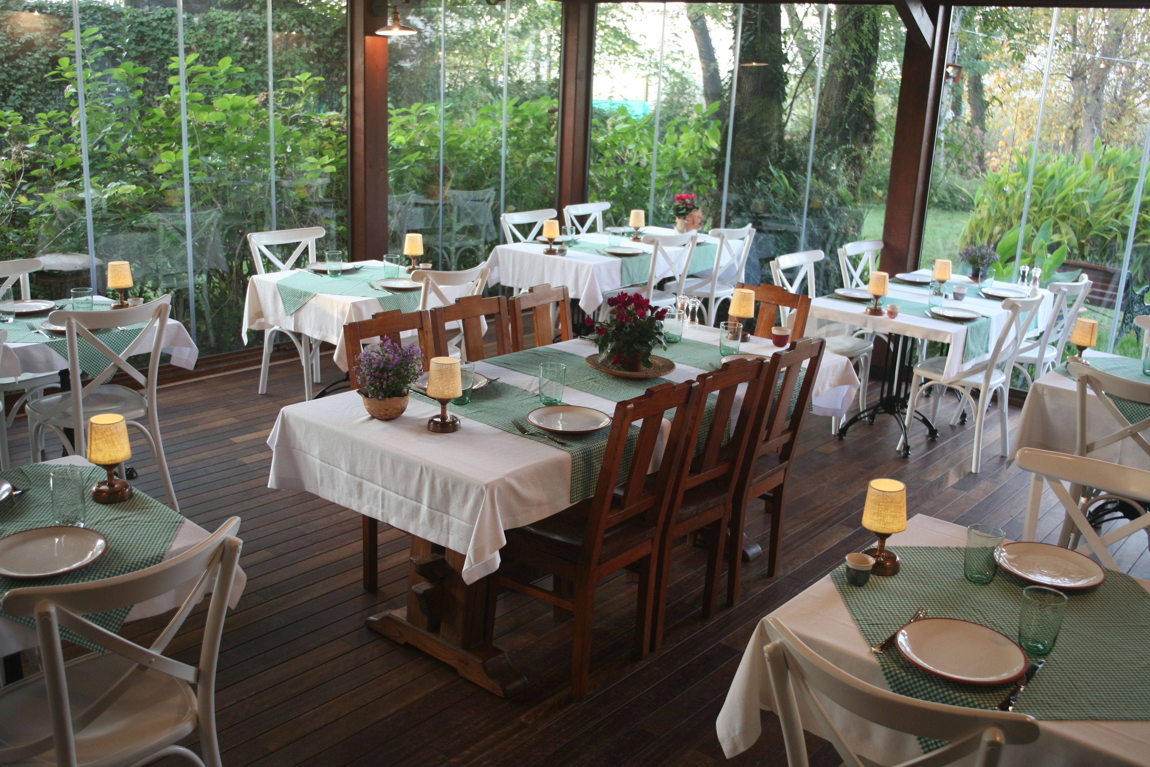 Un restaurante con terraza, mesas y sillas de madera, rodeado de follaje.