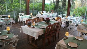 Un restaurante con terraza, mesas y sillas de madera, rodeado de follaje.