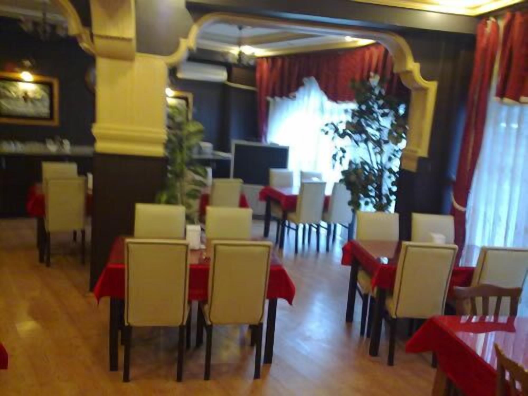 A restaurant with tables set for dining, red tablecloths, and a large plant in the center.
