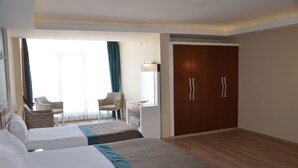 Een hotelkamer met twee bedden, een bureau, een stoel, een kledingkast en een groot raam met gordijnen.