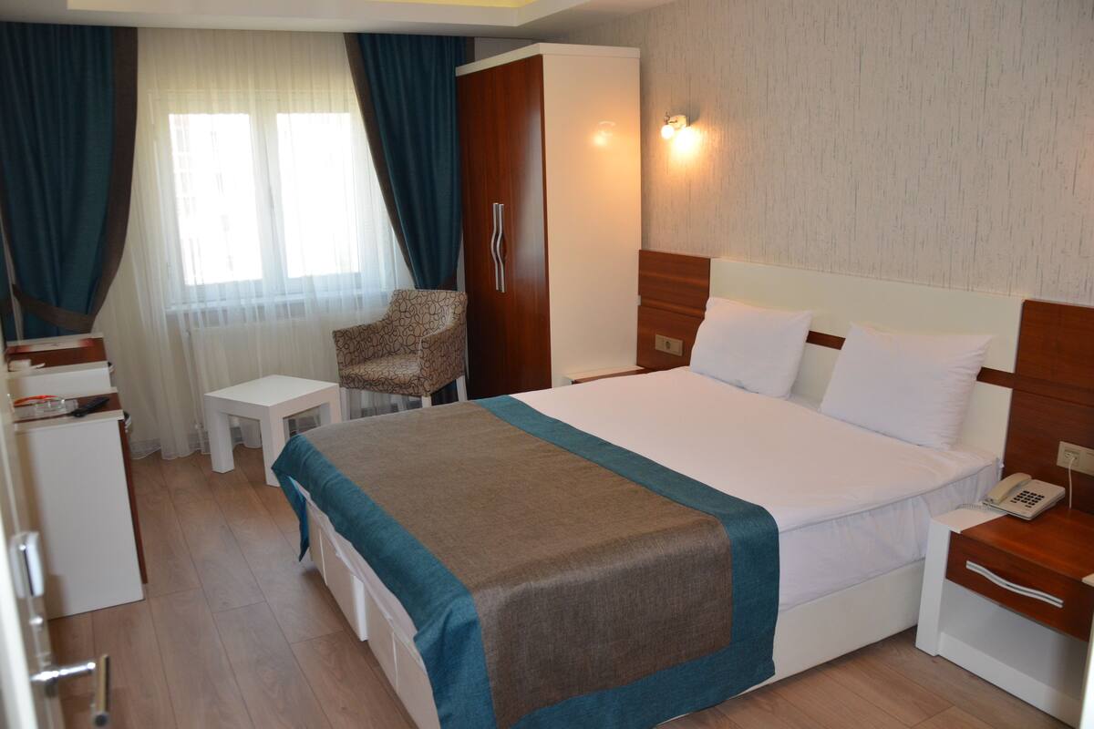 Une chambre d’hôtel comprenant un lit, un bureau, une chaise, une armoire et une fenêtre avec des rideaux.