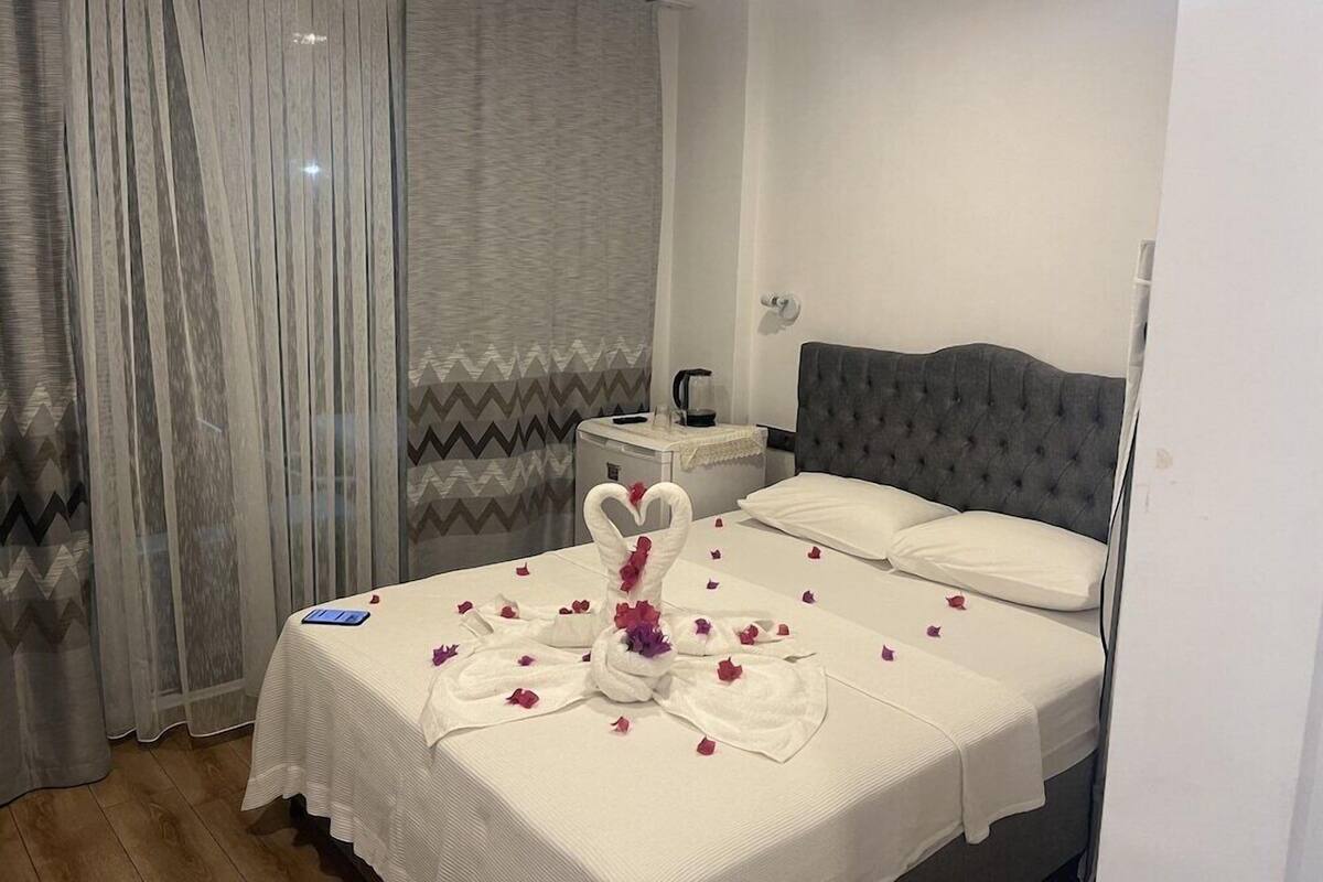 Hotellihuone, jossa on sänky, yöpöytä, vedenkeitin sekä koristeellinen joutsen, joka on tehty pyyhkeistä ja kukista.