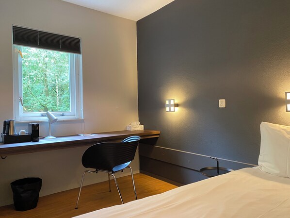 A bedroom with a bed, a desk with a chair, a window with blinds, and two wall-mounted lights. - Hotel Kapellerput Heeze-Eindhoven (Heeze)