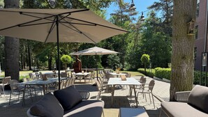 Ein Terrassenbereich im Freien mit Tischen und Stühlen, umgeben von Bäumen und einer Ziegelmauer.