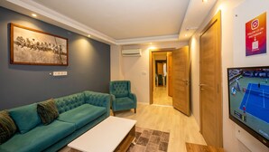 Un salon moderne avec un canapé turquoise, une table basse blanche et un téléviseur diffusant un match de tennis.