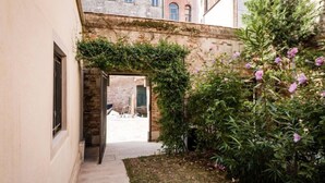 A narrow alleyway with a stone wall, a small garden with purple flowers, and a building entrance. - MYSWEETPLACE - Fondamenta Moro Apartment (Venice)