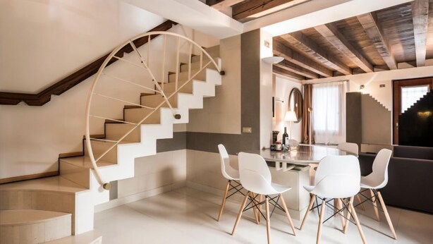 A modern interior with a spiral staircase, a dining area with white chairs, and a dark-colored sofa. - MYSWEETPLACE - Fondamenta Moro Apartment (Venice)