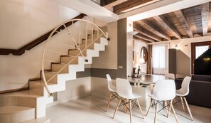 A modern interior with a spiral staircase, a dining area with white chairs, and a dark-colored sofa. - MYSWEETPLACE - Fondamenta Moro Apartment (Venice)