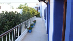 Un balcone stretto con pareti blu, ringhiere bianche, piante in vaso e una vista aperta sul cielo.