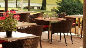 Ein Essbereich im Freien mit Tischen und Korbstühlen, umgeben von einer Pergola mit weißem Baldachin.