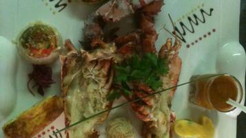 A seafood platter with a lobster, shrimp, and various sauces on a white plate.