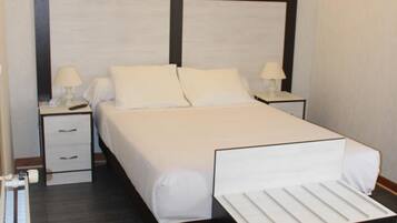 Camera d'albergo con un letto grande, due comodini con lampade, un tavolino e una panca integrata ai piedi del letto.