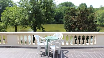 Una terraza con sillas blancas y una mesa, con vistas a un estanque rodeado de árboles.