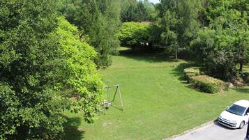 A residential area with a grassy lawn, a swing set, and a white car parked on the street.