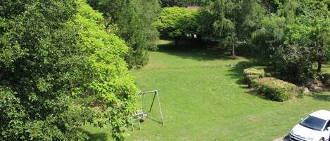 A residential area with a grassy lawn, a swing set, and a white car parked on the street.