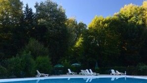 Ein Schwimmbecken mit weißen Liegestühlen und üppiger Bepflanzung im Hintergrund.