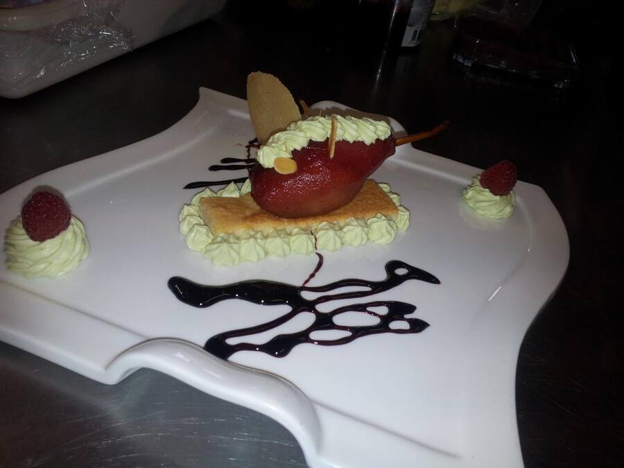 Un dessert servi dans une assiette blanche, accompagné de crème fouettée, de quelques fruits rouges et d’un filet de chocolat.