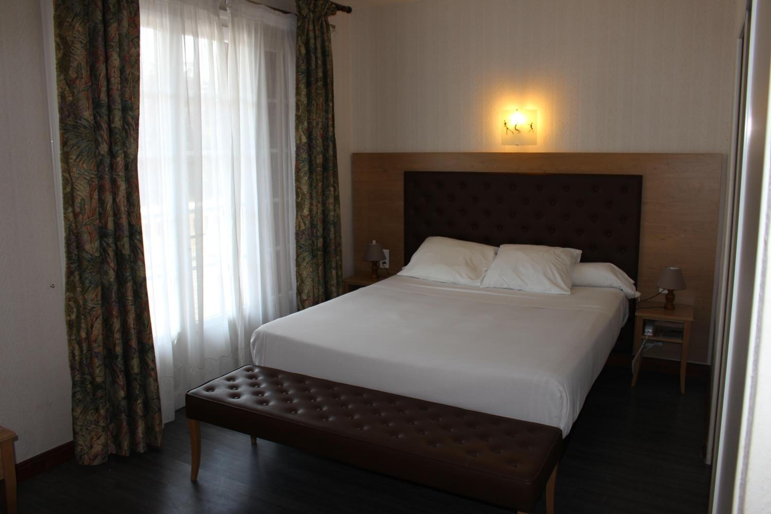 Habitación de hotel con una cama grande, una banca, una mesita de noche con lámpara y un aplique de pared.