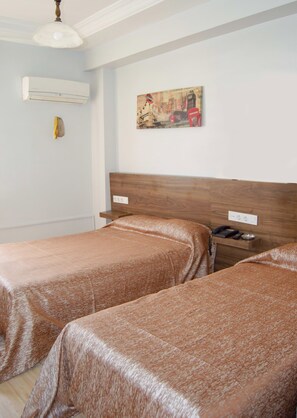 A hotel room with two beds, a wooden headboard, a painting on the wall, and a bedside table with a phone and a bowl. - Yunus Hotel (Gaziantep)