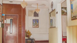 Um hall de hotel com piso lustroso, um balcão de recepção, um candelabro e um relógio fixado na parede.
