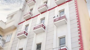 Um hotel com várias varandas, uma bandeira visível e uma placa indicando ser o Yunus Hotel.