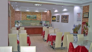 Restaurante com parede de tijolos, balcão e várias mesas com cadeiras.