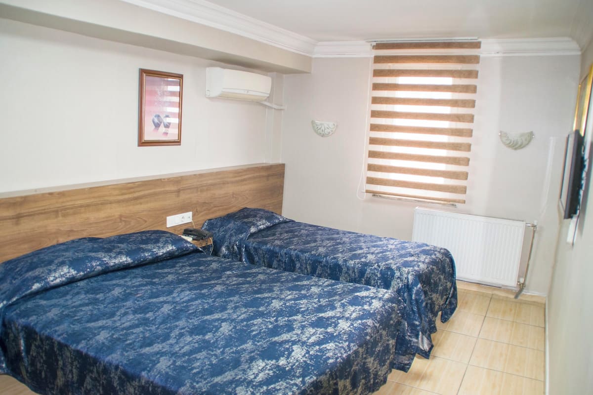 Un dormitorio con dos camas, cabeceros de madera, un radiador y una ventana con persianas.