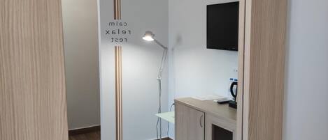 A hallway with a wooden floor, a desk with a lamp, and a mounted TV.