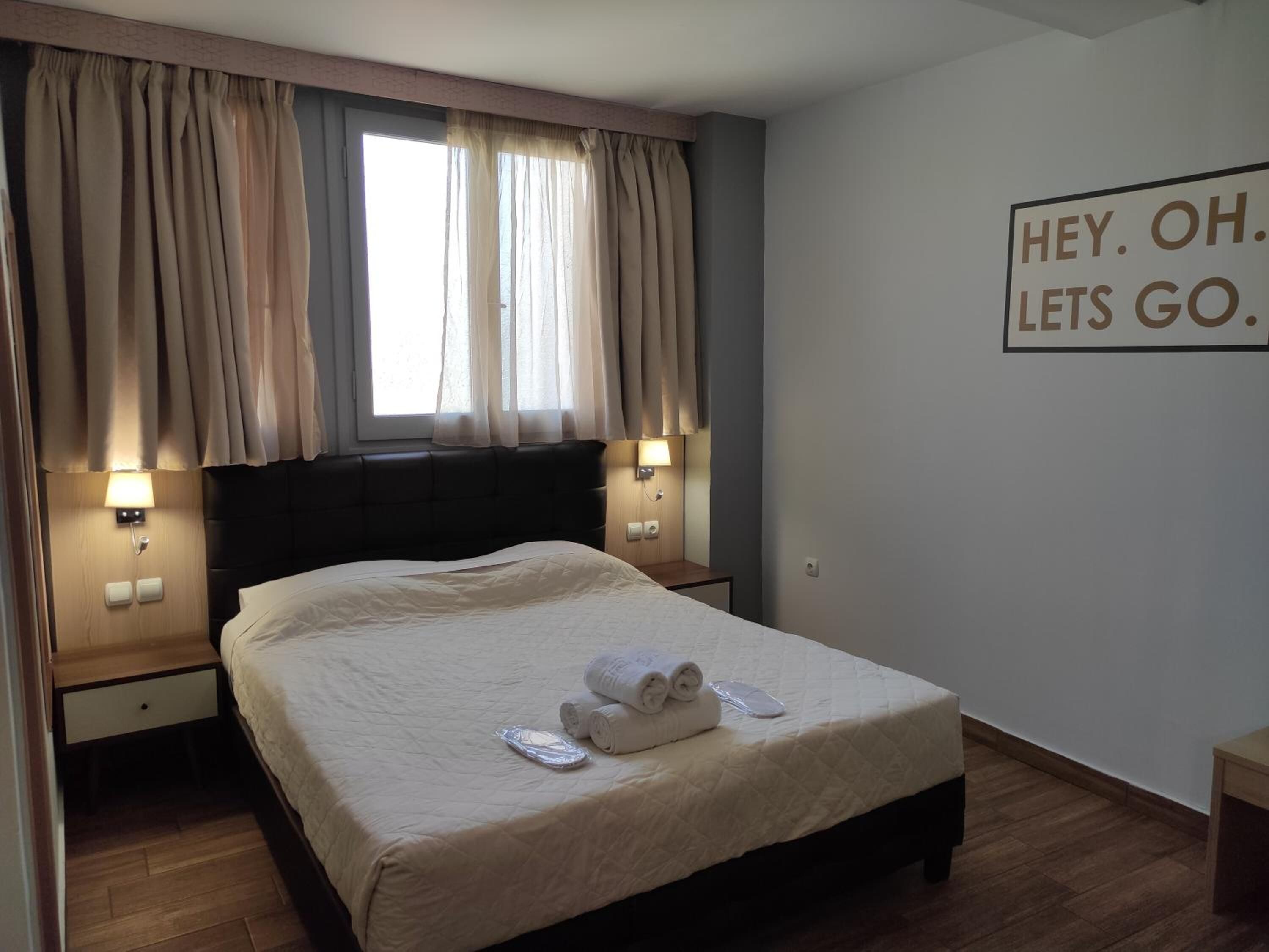 Una cama bien hecha con cabecera, dos lámparas de noche y una ventana con cortinas.