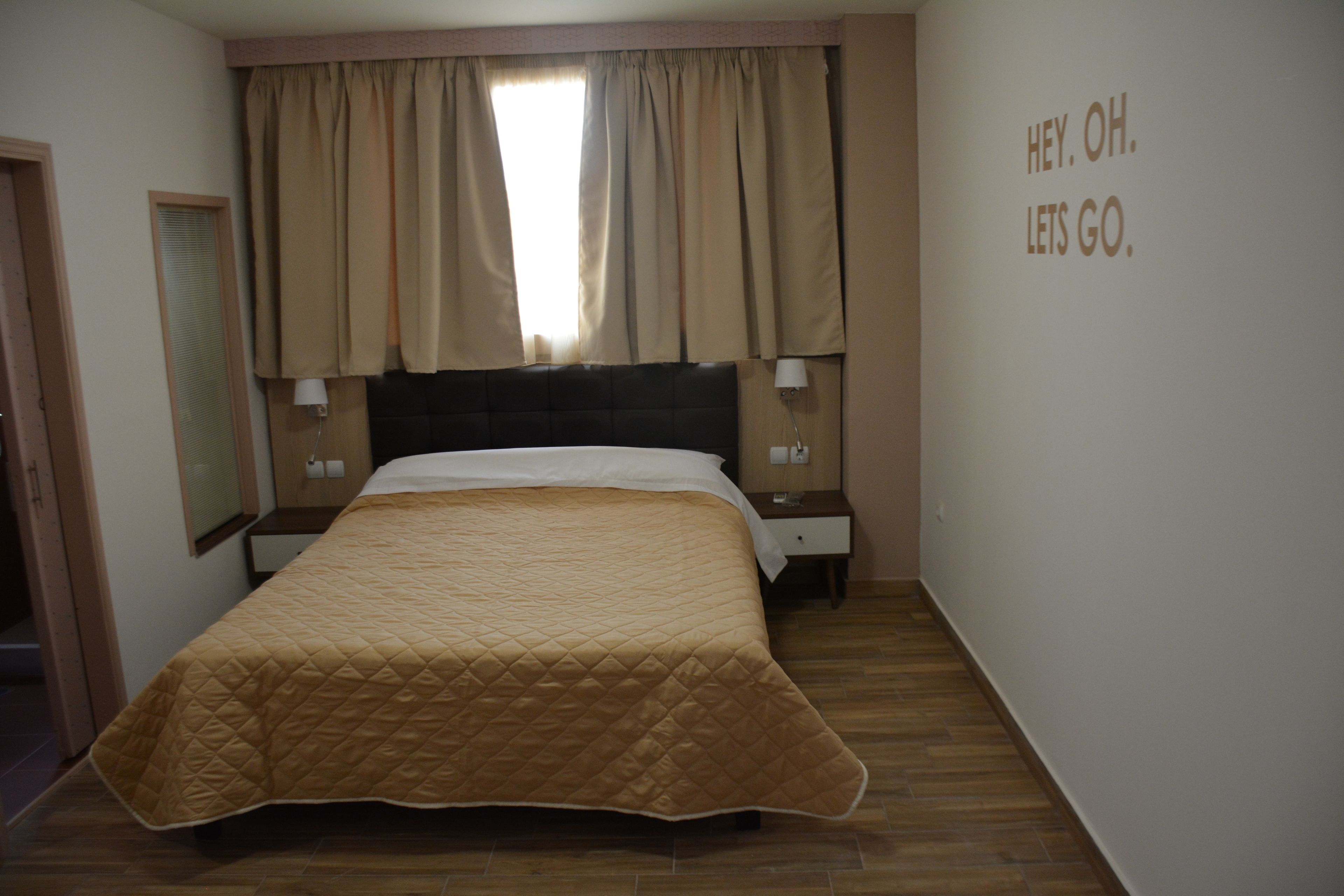 Une chambre d’hôtel avec un grand lit, une table de chevet, une lampe et une fenêtre avec des rideaux.
