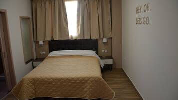 Une chambre d’hôtel avec un grand lit, une table de chevet, une lampe et une fenêtre avec des rideaux.