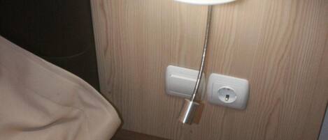 A wooden nightstand with a lamp, a brochure titled "Chios Xios," and a power outlet.